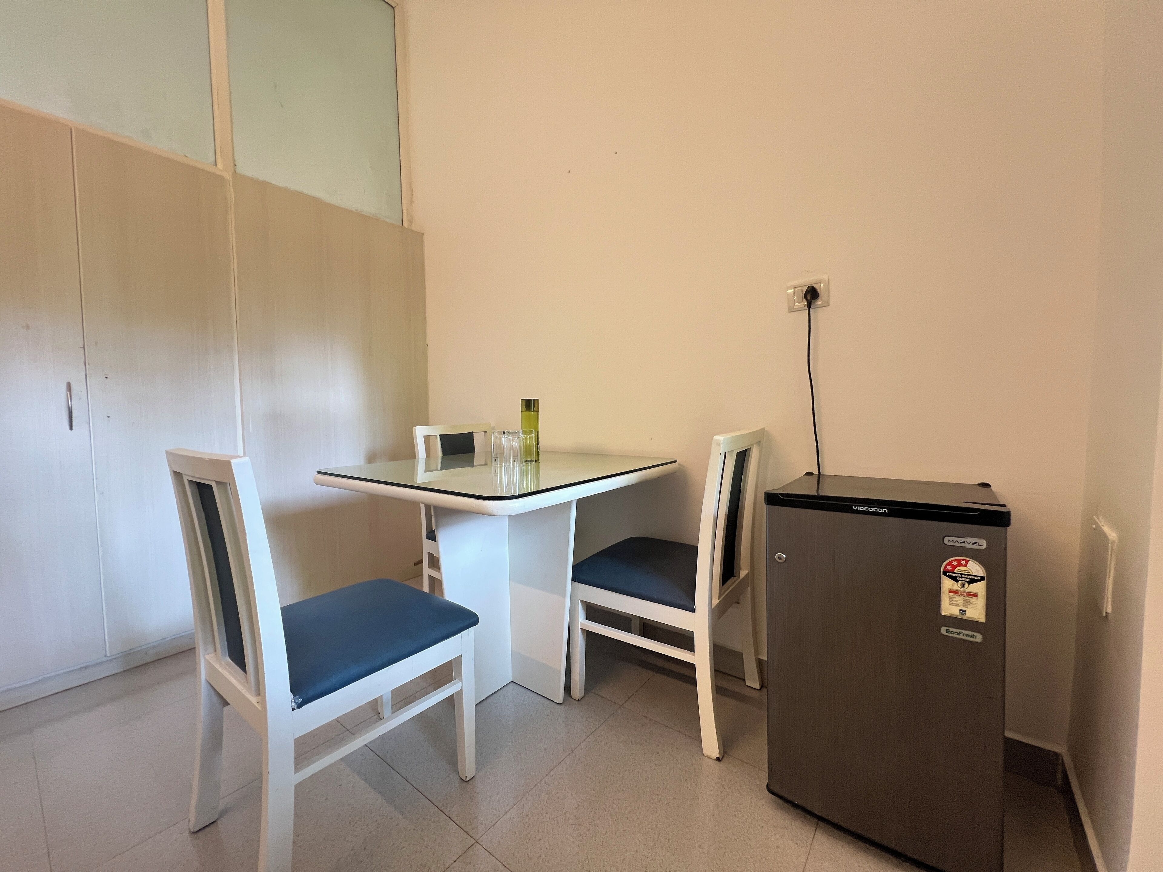 A small kitchenette with a table and two chairs, a refrigerator, and a wall-mounted power outlet.