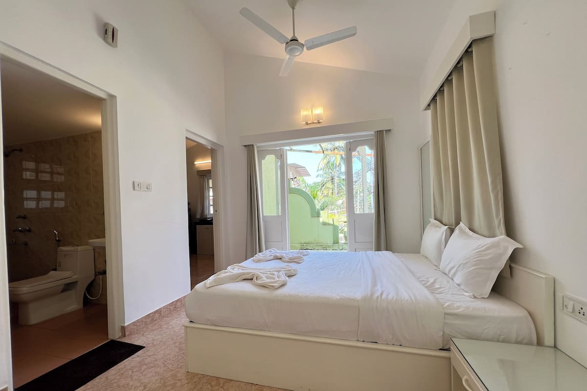 A bedroom with a bed, a bedside table, a ceiling fan, and a view of the outside.