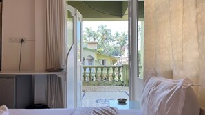 A hotel room with a bed, a small table with a bowl, a TV, and a view of a courtyard with palm trees. - Gaur Opulent Goa (Candolim)