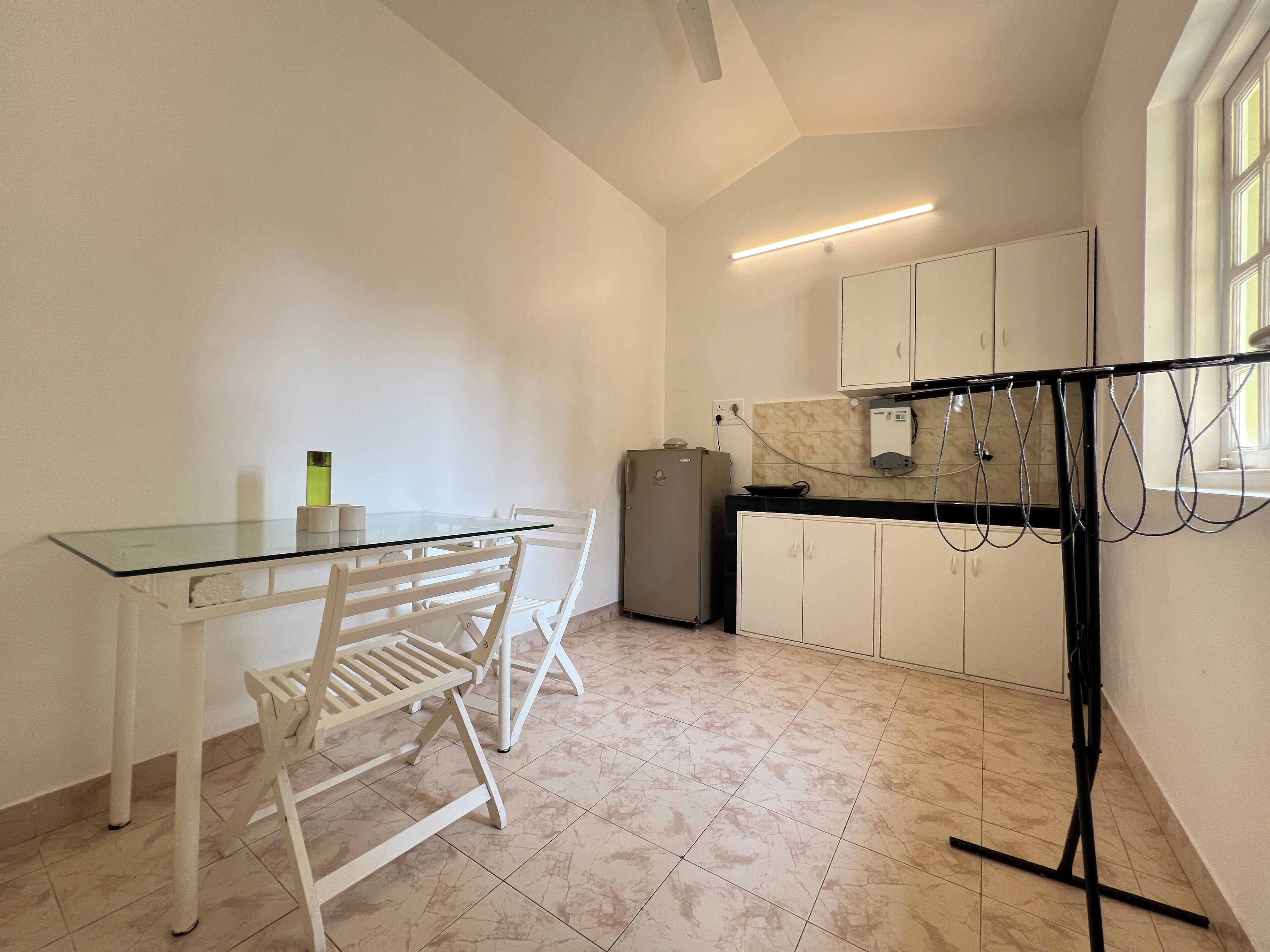 Een kleine keuken met witte kastjes, een tafel met glazen blad en een witte stoel.
