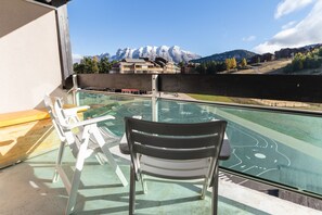 A balcony with a glass table and chairs, overlooking a pool and a mountainous landscape. - Ski-front apartment, sleeps 5 (Le Dévoluy)