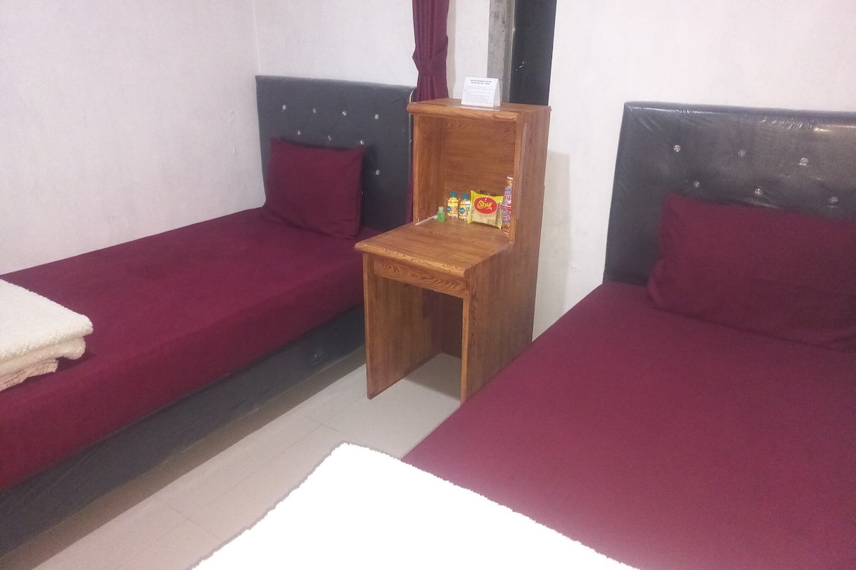 Una habitación con dos camas individuales, cada una con una mesita de noche de madera y una colcha roja.