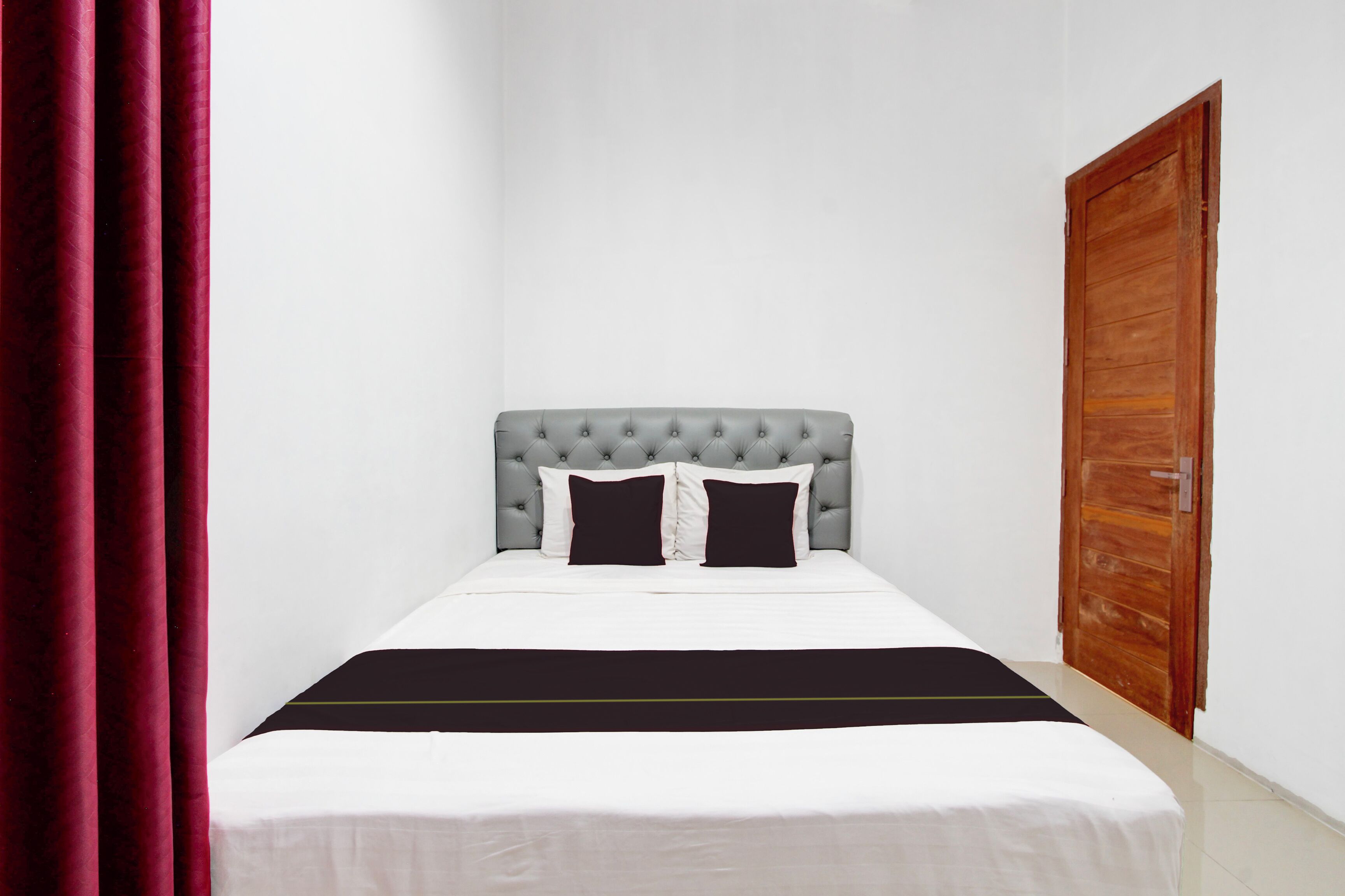 A neatly made bed with a grey tufted headboard, white bedding, and a black accent strip.