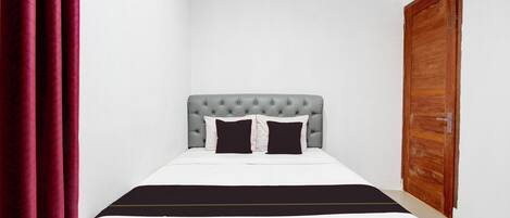 A neatly made bed with a grey tufted headboard, white bedding, and a black accent strip.