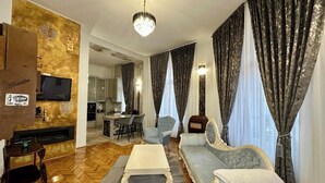 A living room with a sofa, armchairs, a coffee table, and a TV. There is a kitchen in the background. - 1 Bed Royal Escape - City Central, Wifi (Arad)