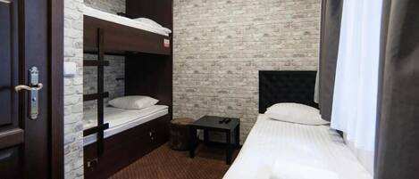 A hotel room with a bunk bed, a single bed, a small table, and a brick-patterned wall.