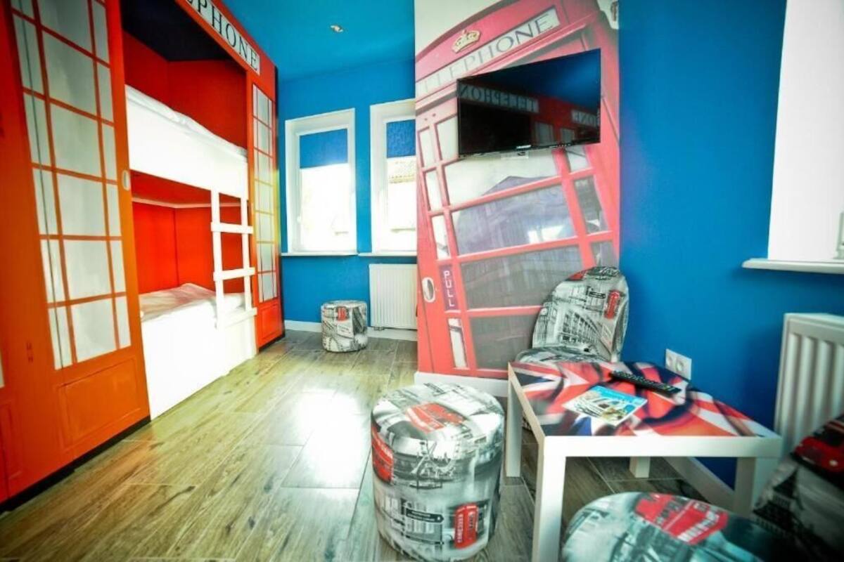 A room with a blue and red color scheme, featuring a bunk bed, a table with magazines, and a window with a red telephone booth design.