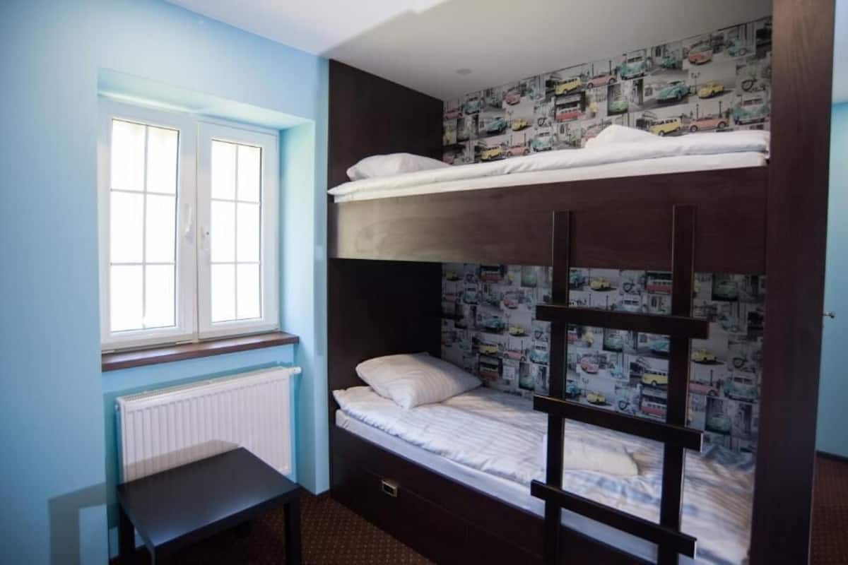 A bunk bed room with a window, a radiator, and a wall with a car-themed wallpaper.