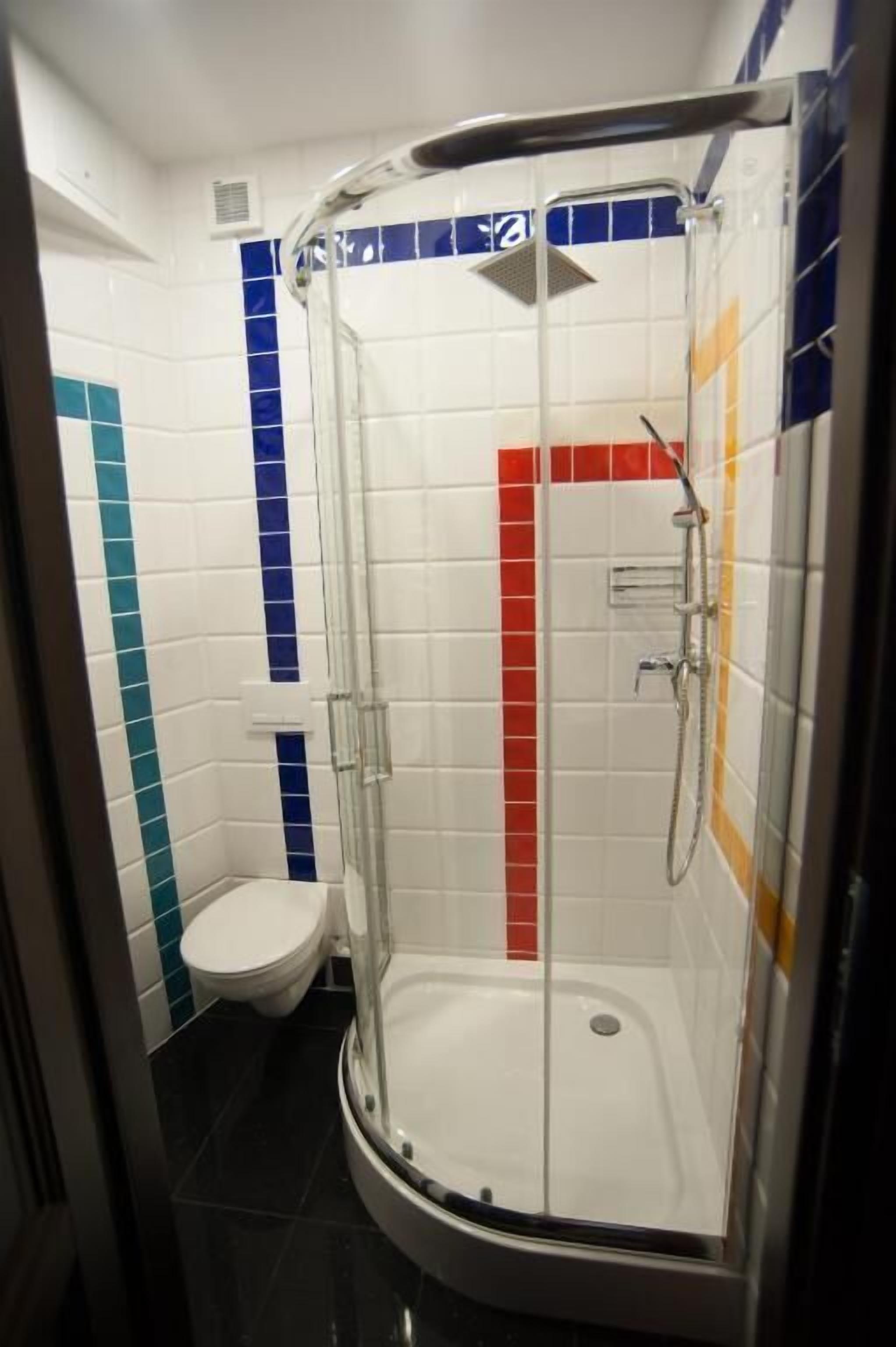 Una cabina de ducha con puerta de vidrio, junto a un inodoro en un baño con paredes de azulejos y suelo negro.