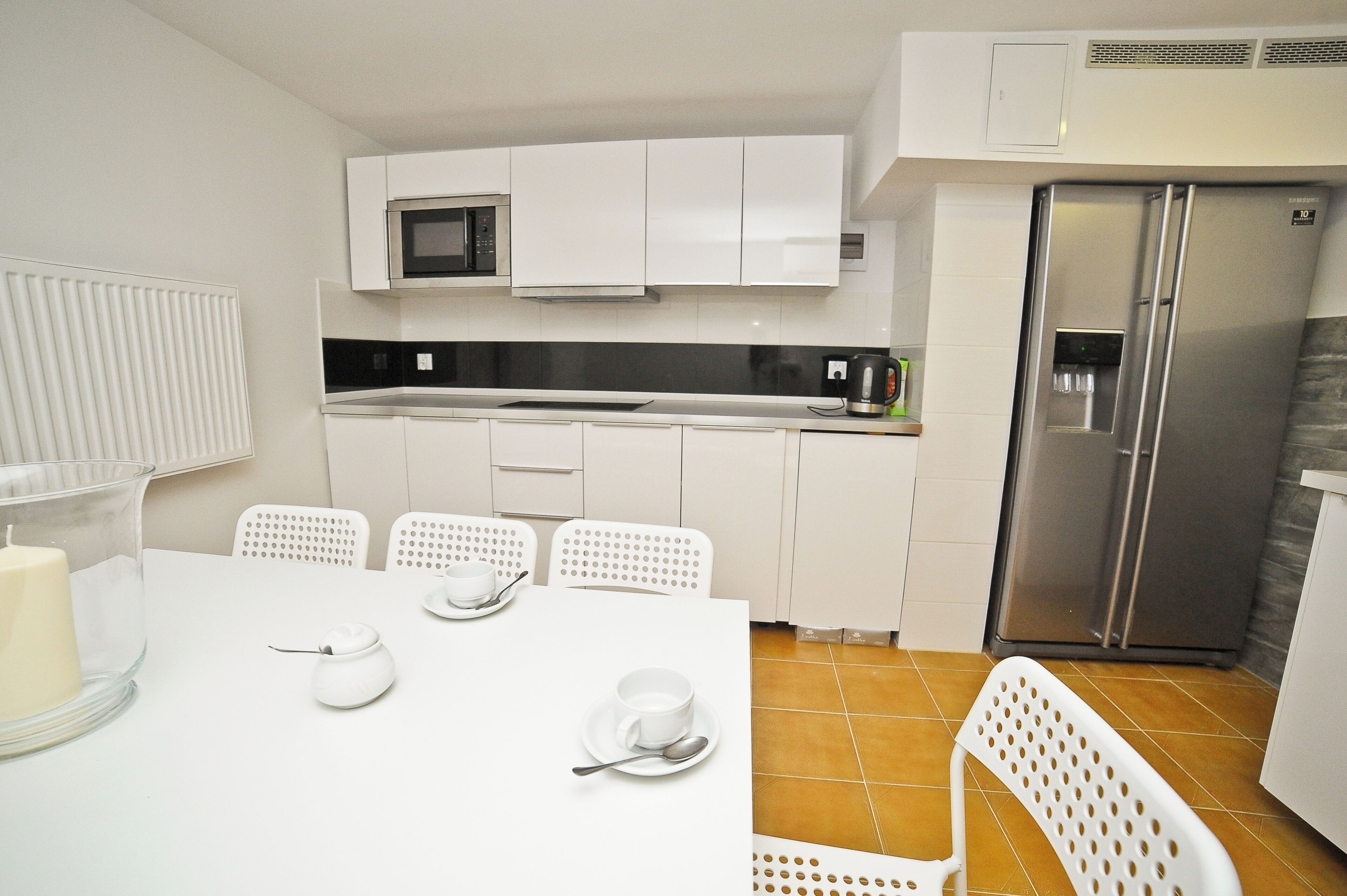 Una cocina moderna con gabinetes blancos, un refrigerador de acero inoxidable, un microondas y un comedor con una mesa y sillas blancas.