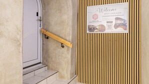 A staircase with a wooden handrail leading to a door with a keypad lock. A welcome sign with a QR code and text is displayed on the wall.