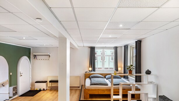 A room with a bed, a window, a radiator, a bench, and a door.