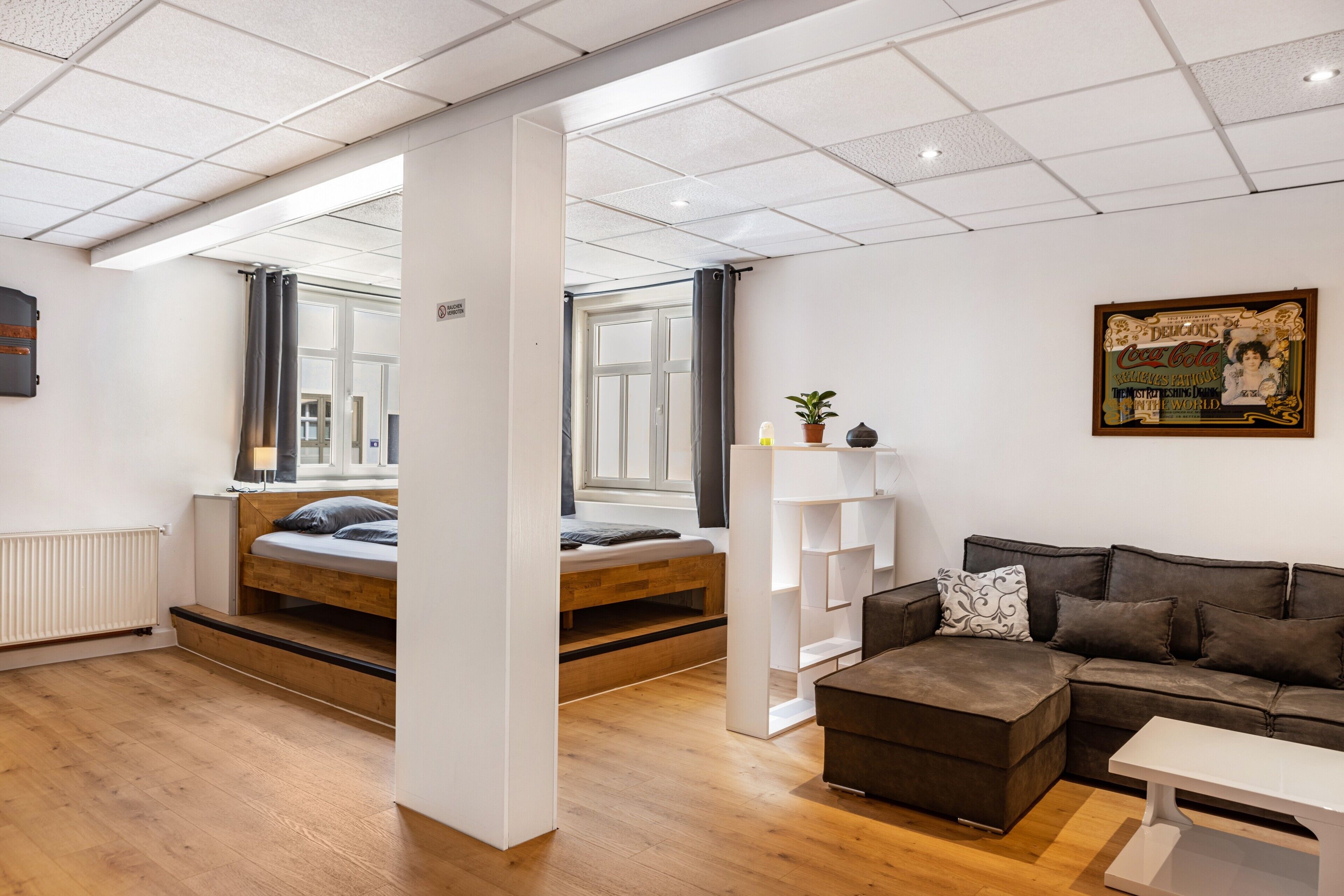 A modern room with a bed, a sofa, a coffee table, a plant, and a wall-mounted shelf.
