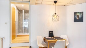 A modern interior with a glass shower, a dining table with chairs, a pendant light, and a framed picture on the wall.