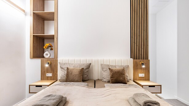 A modern bedroom with a bed, two nightstands, a wooden shelf, and a wall-mounted light fixture. - City Loft Kurfürstendamm | Walk to Everything (3) (Berlin)