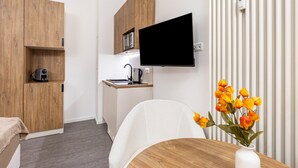 A compact room with a kitchenette, a flat-screen TV mounted on the wall, a wooden dining table, and a white chair. - City Loft Kurfürstendamm | Walk to Everything (3) (Berlin)