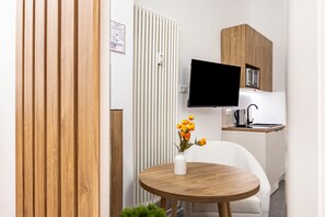 A modern kitchen with a flat-screen TV, a white chair, and a wooden table with a vase of flowers. - City Loft Kurfürstendamm | Walk to Everything (3) (Berlin)