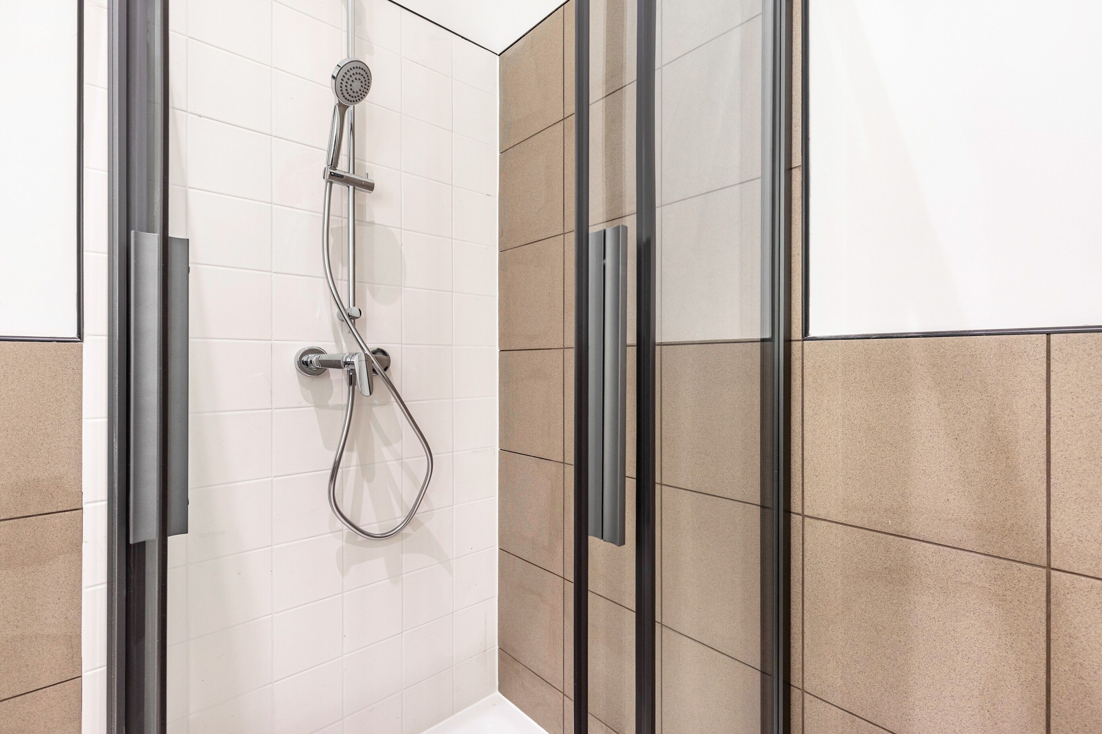 A modern shower with a glass enclosure, a handheld showerhead, and a wall-mounted control panel.