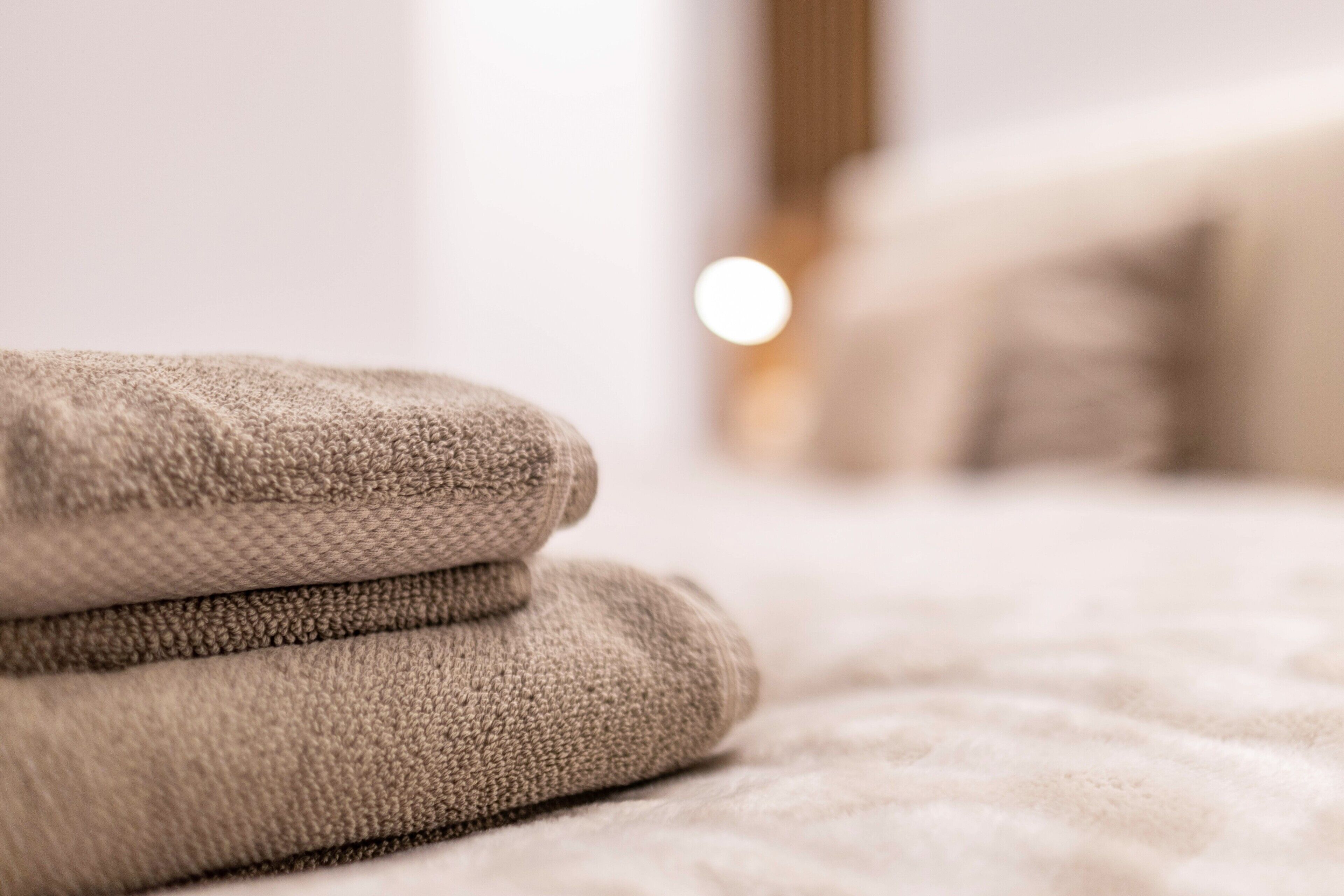 A neatly folded beige towel on a bed with a blurred background.