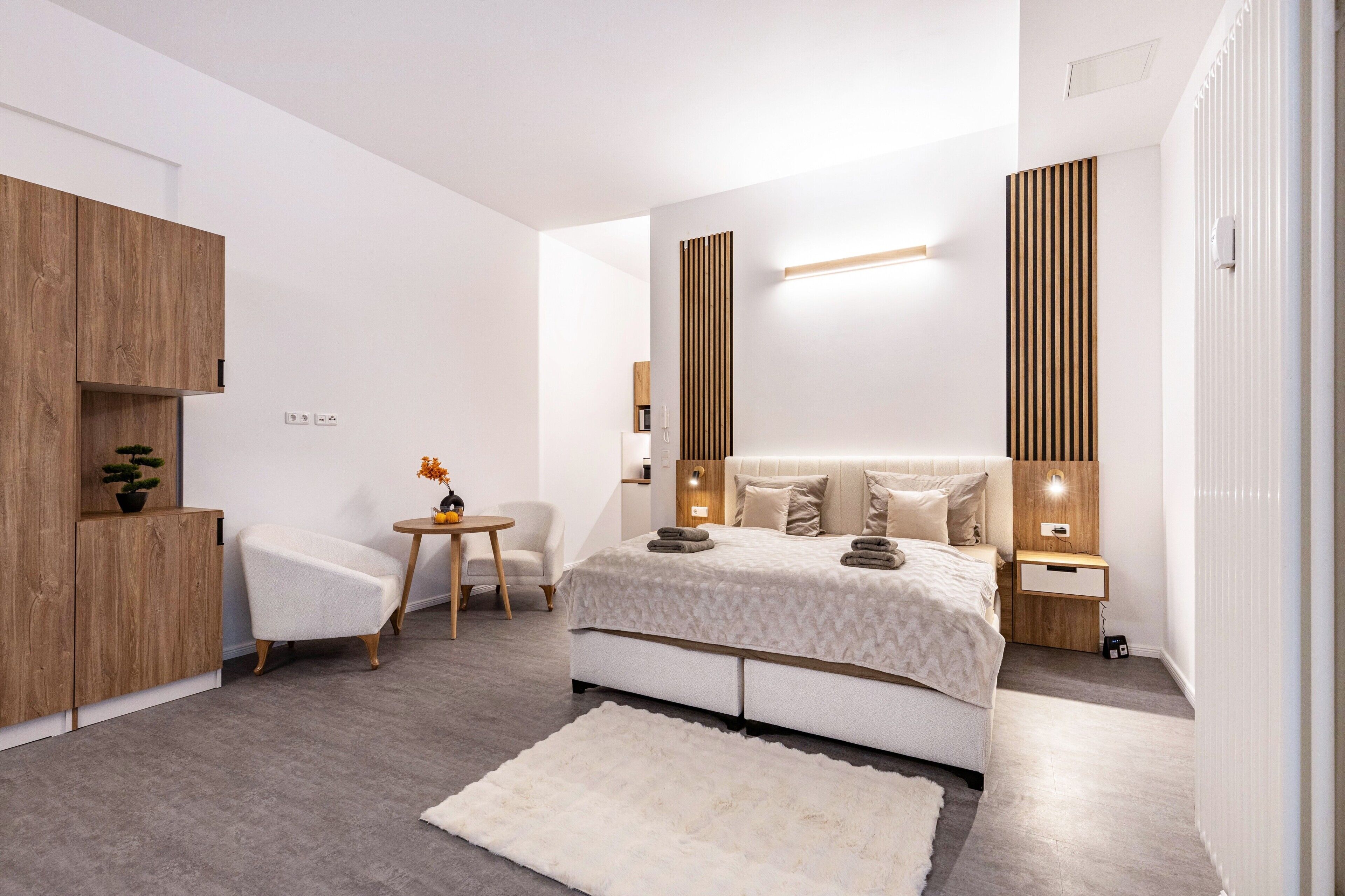 Um quarto moderno com uma cama, mesas de cabeceira, uma cadeira e uma pequena mesa com uma planta.