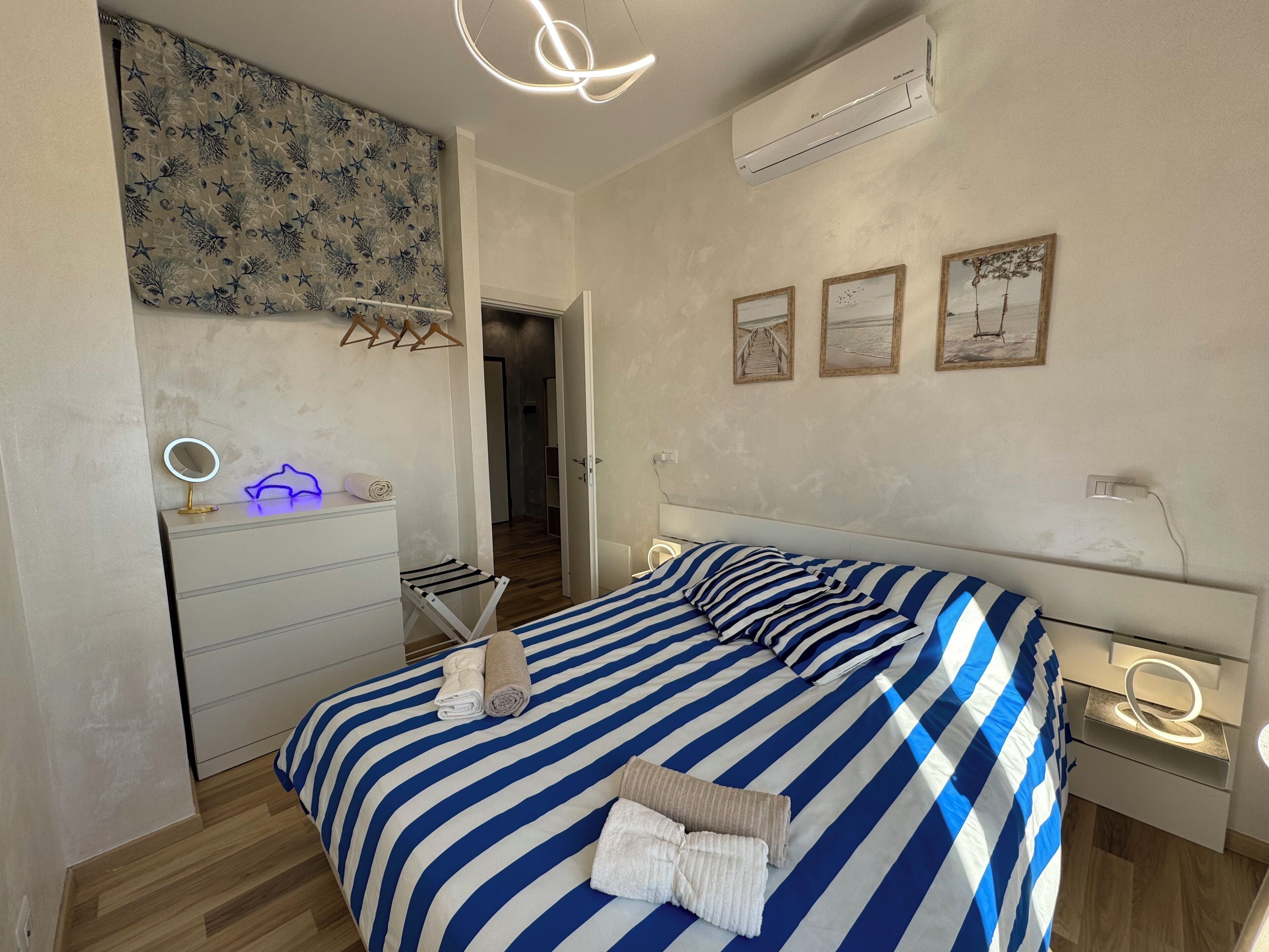 Ein Schlafzimmer mit einem Bett, Nachttischen, einem Spiegel, einem hängenden Handtuchhalter und einer Wand-Klimaanlage.