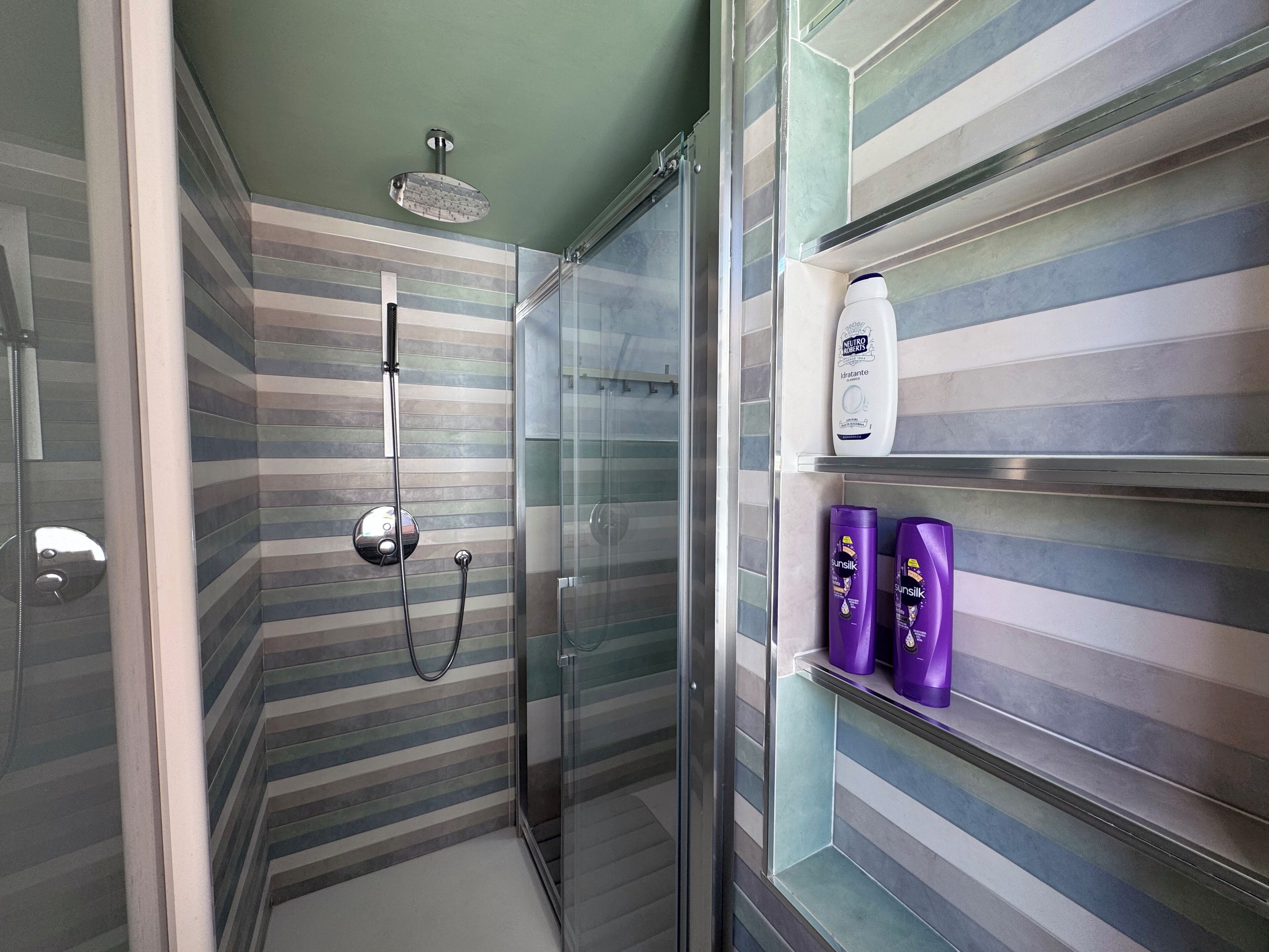 Une salle de bain moderne avec une douche à parois de verre, des carreaux de mur à rayures et une étagère contenant des articles de toilette.