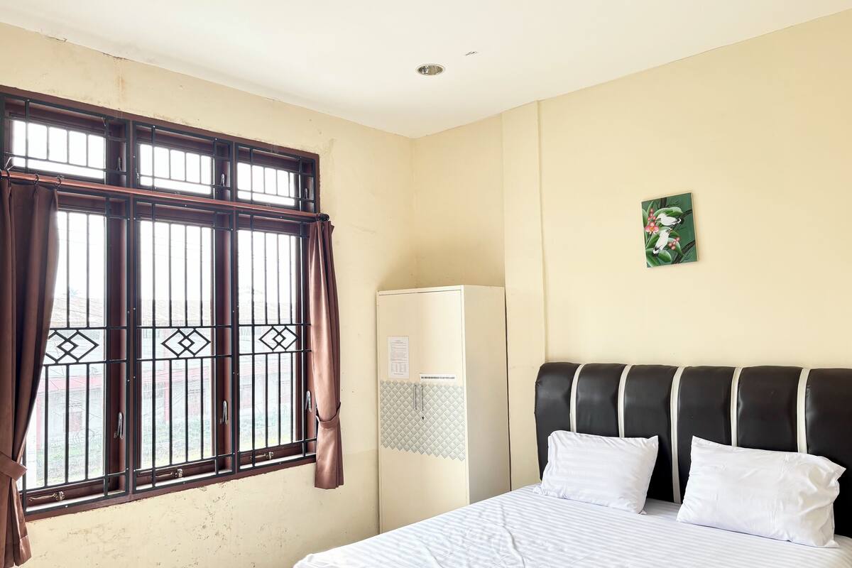 Una habitación de hotel con cama, armario, ventana con cortinas e imagen colgada en la pared.