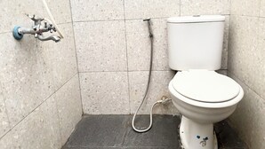 Un baño pequeño con azulejos, un inodoro, un cabezal de ducha manual y un grifo empotrado.