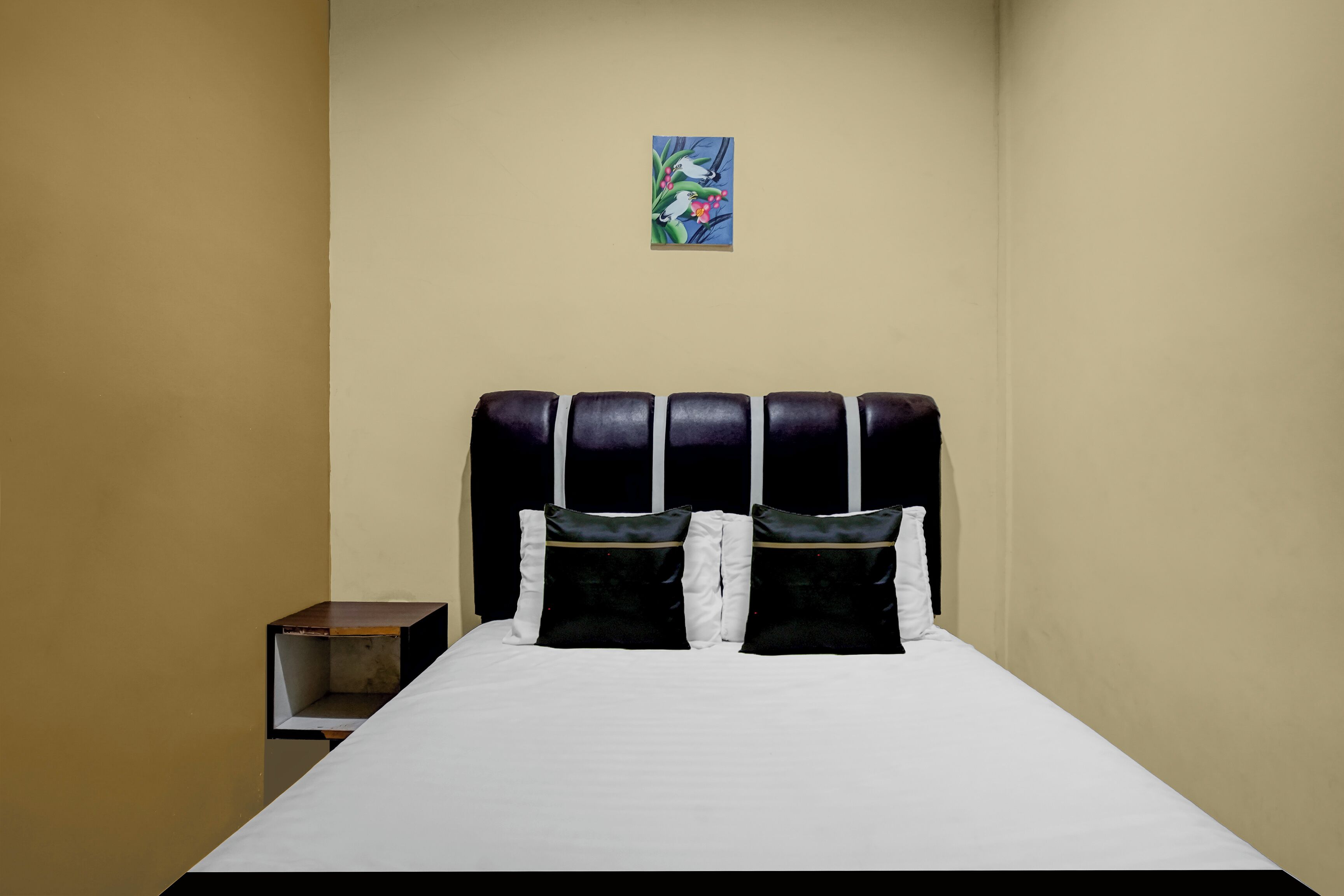A neatly made bed with a black headboard, white bedding, and two black pillows with white trim.