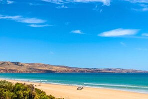 A beach with a clear sky, a sandy shore, and distant hills. - Aldinga Stunning Sea View – 2BR Retro Vibe (Aldinga Beach)