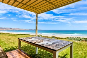 A wooden table with a glass of wine and a napkin, set on a grassy area with a view of the beach and ocean.