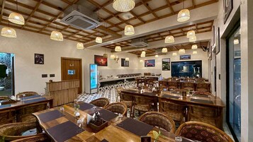 Un restaurante con varias mesas y sillas, un refrigerador y lámparas colgantes.