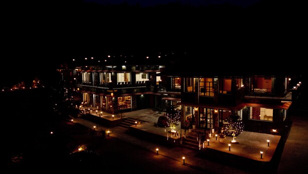 Un edificio a più piani con finestre illuminate e illuminazione esterna, che presenta un cortile centrale con un albero di Natale e una zona relax.