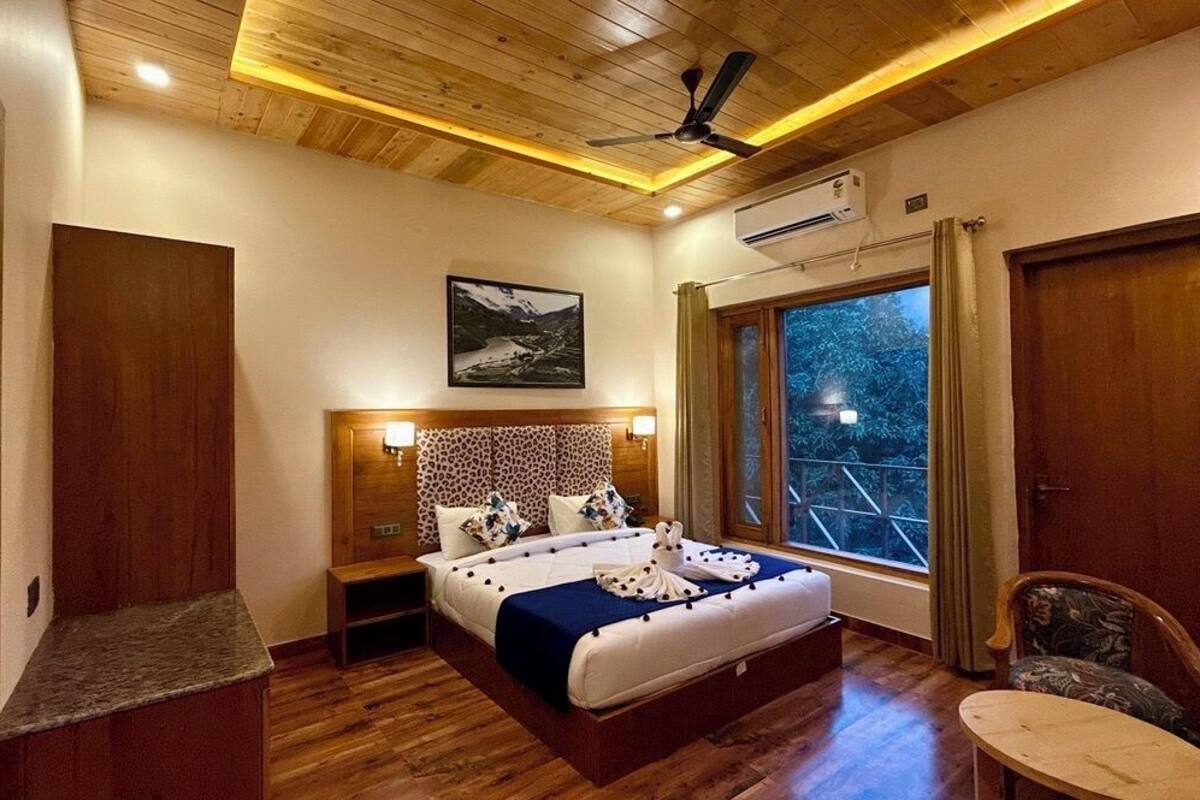 Une chambre avec un plafond en bois, un lit avec une tête de lit, des lampes de chevet, une fenêtre donnant sur un beau paysage et un fauteuil.
