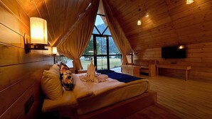 Camera da letto in una baita di legno, con un letto, una TV e un'ampia finestra.