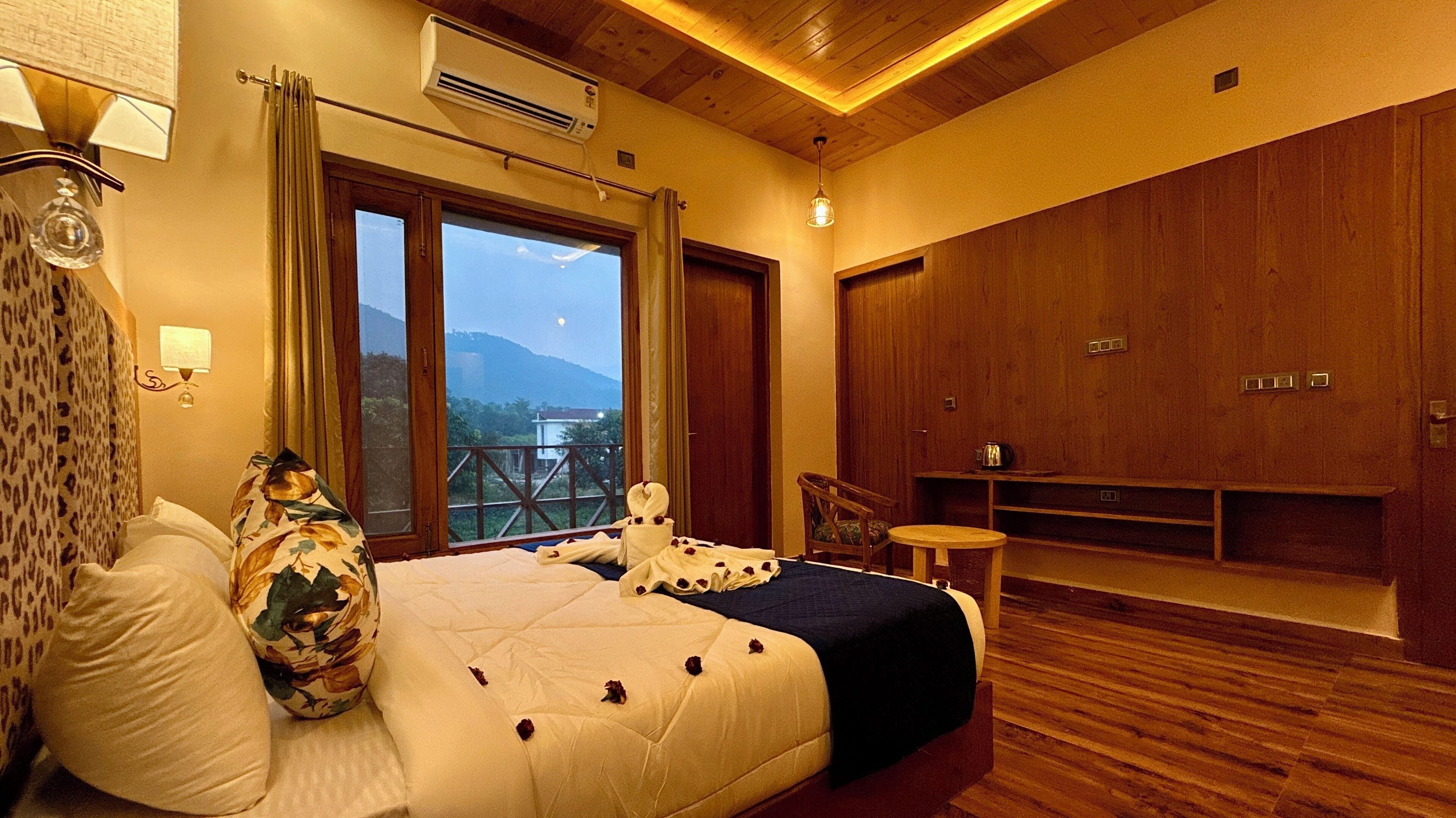A bedroom with a large bed, a wooden wardrobe, a small table, and a view of the outdoors.