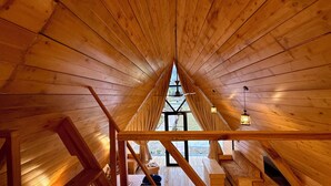 Un interno in legno con soffitto spiovente, travi a vista e una finestra.