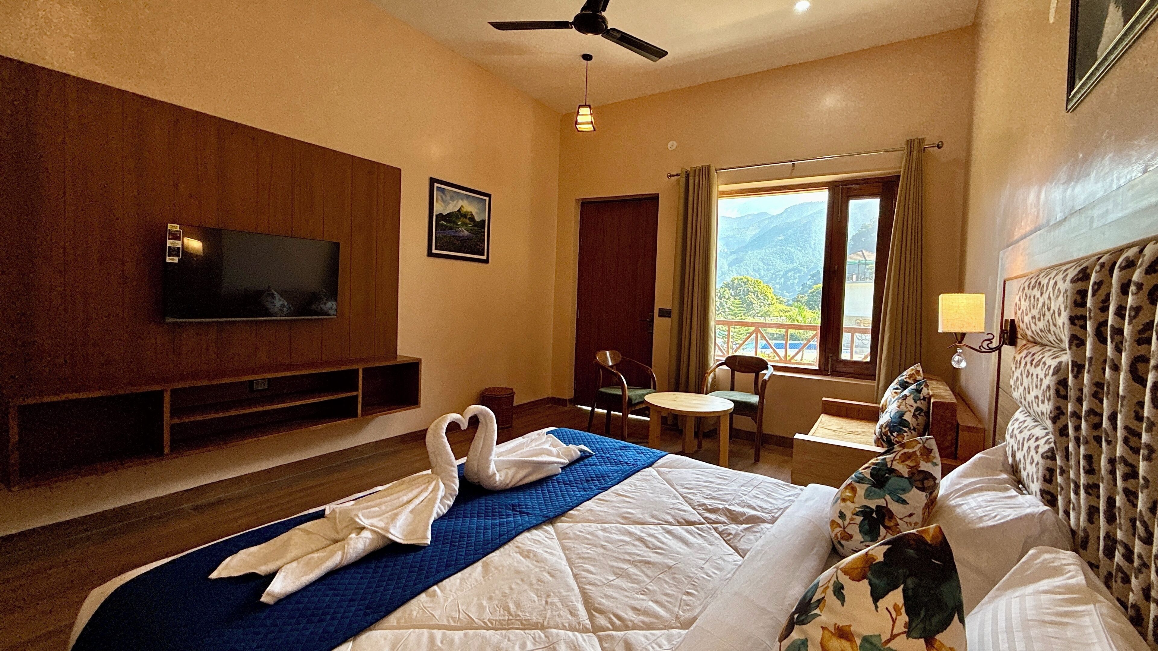 A hotel room with a bed, a television, a desk, a chair, and a window with a mountain view.