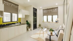 A modern kitchen with a sink, cabinets, and a window. There is a small table with a plant and a book. The room has a sofa and a window with a view. - Nguyen Homestay Phan Ton - District 1 (Ho Chi Minh City)