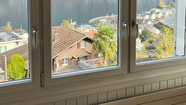 A room with three windows overlooking a lake and a town.