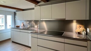 A modern kitchen with light grey cabinets, a stainless steel countertop, and wooden beams on the ceiling.