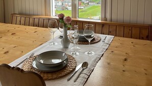 A dining table set with plates, glasses, and cutlery, with a view of mountains and a village through a window.
