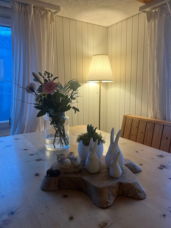 A dining table with a vase of flowers, a lamp, and decorative bunny figures. - Cozy vacation apartment with lake and alpine view - Flumserberg ski area (Quarten)