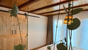 A bedroom with a wooden ceiling, a bed with white bedding, and a hanging plant with green leaves.