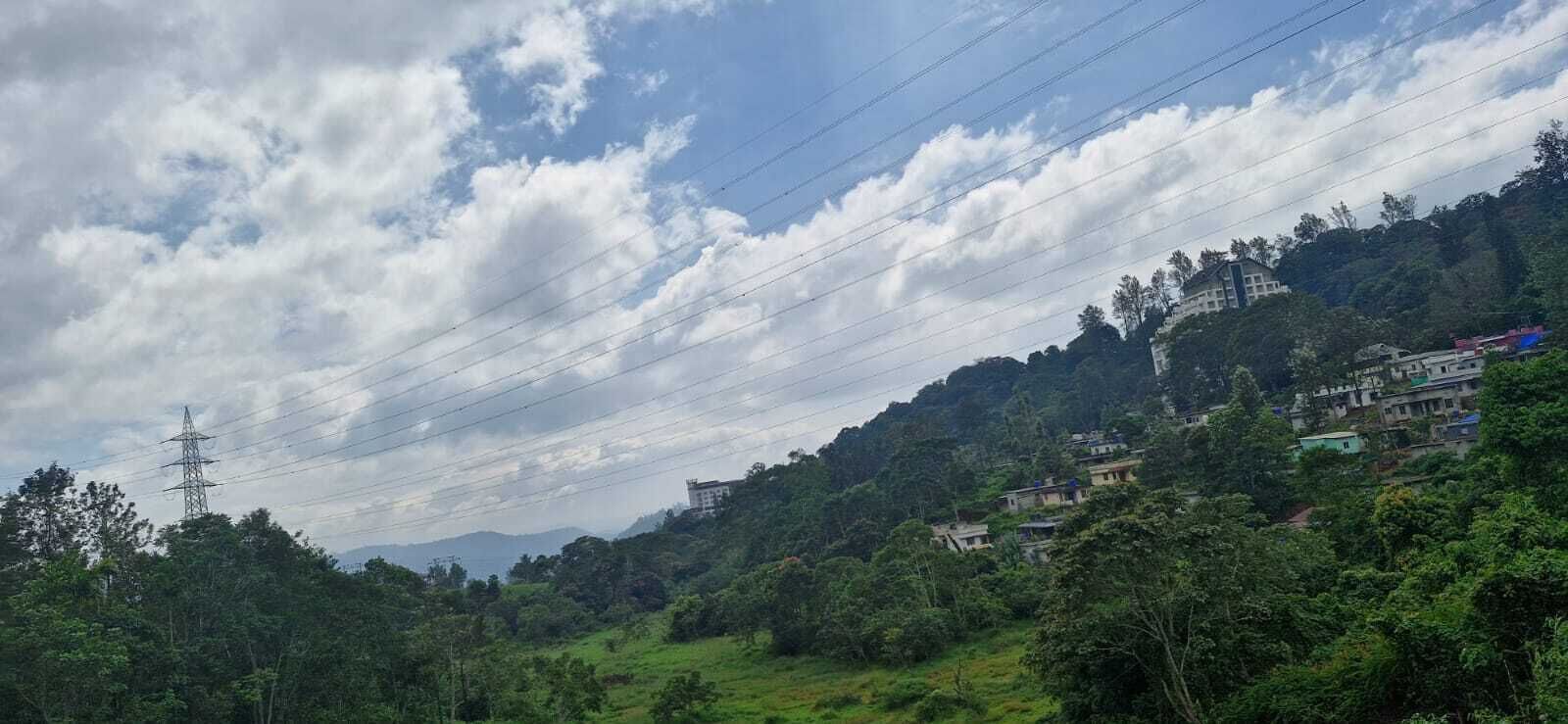 A hilly landscape with scattered buildings, power lines, and dense greenery.