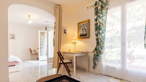 Une chambre d’hôtel avec un lit, un bureau, une chaise, une lampe et une vue sur la verdure environnante.
