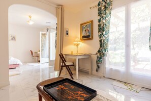 Une chambre d’hôtel avec un lit, un bureau, une chaise, une lampe et une vue sur la verdure environnante.