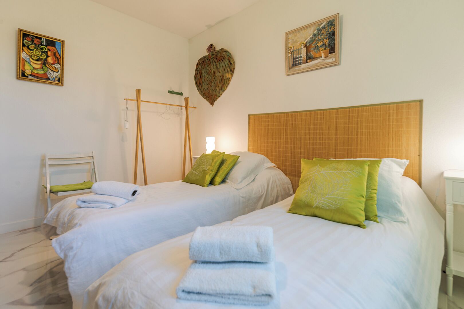 Een hotelkamer met twee bedden, een houten hoofdbord, een hangplant en kunst aan de muren.