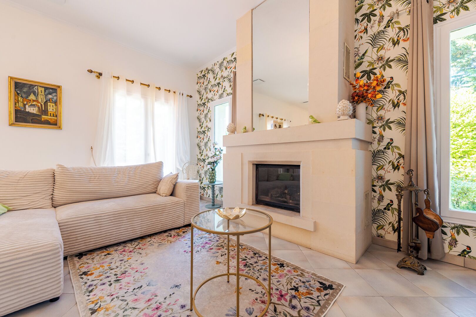 A living room with a sofa, a fireplace, a round glass table, and a floral-patterned rug.
