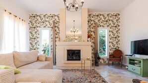 Un salon avec une cheminée, un canapé, un téléviseur et un papier peint à motifs floraux.
